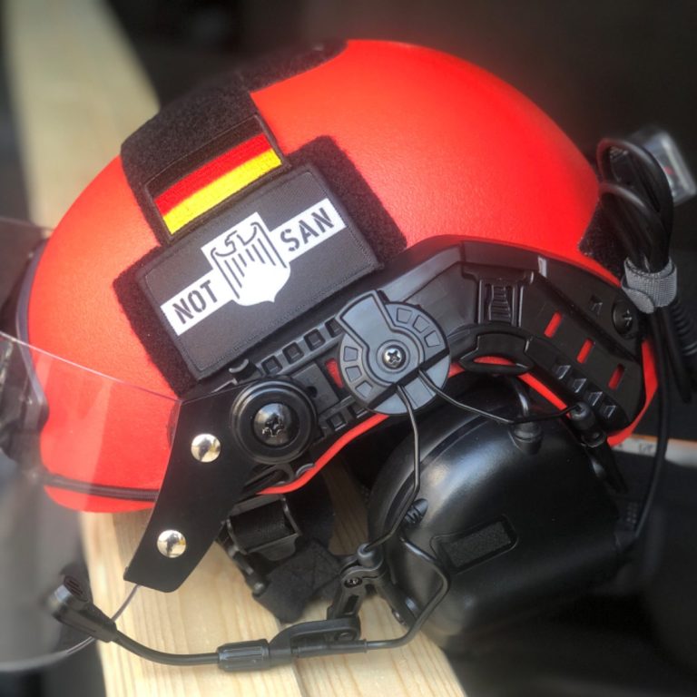 Ein Roter Helm mit der Aufschrift Not-San, einem Visier und einem Gehörschutz