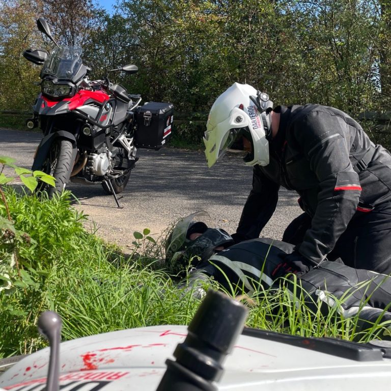 Ein Motorradfahrer liegt verletzt im Straßengraben. Ein anderer kniet über ihm und versorgt ihn