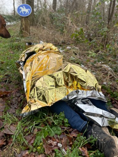Eine Person liegt eingewickelt in einer Rettungsdecke auf einem Reitweg