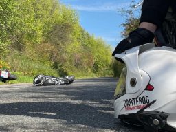 Eine Unfallstelle wird mit einem Helm abgesichert. Ein Verletztendarsteller liegt mit seinem Motorrad im Straßengraben 