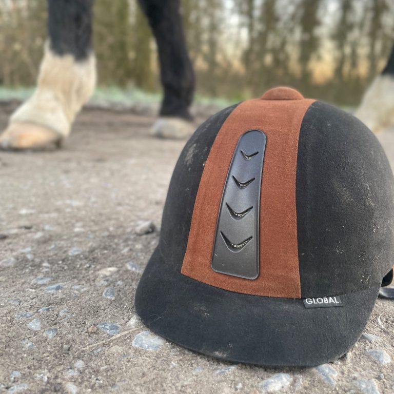 Ein Reithelm liegt auf dem Boden. Hufe eines Pferdes sind im Hintergrund zu sehen