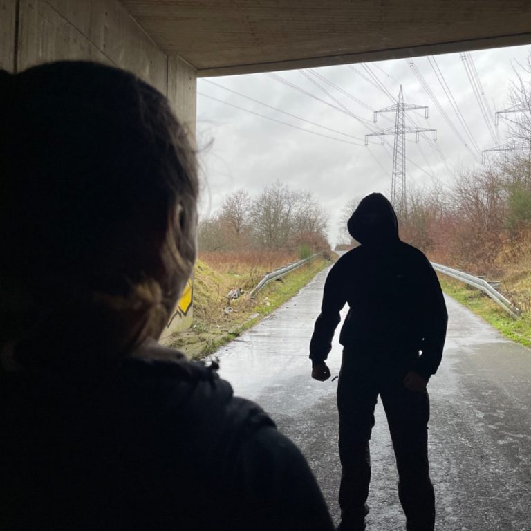 Eine Frau steht in einem dunklen Tunnel und wird von einer im Schatten stehenden Mann bedroht