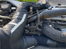 DRRS Motorradunfall Ein darstellender Motorradfahrer liegt unter seinem Motorrad eingeklemmt