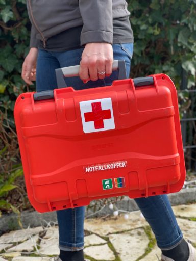 Eine Person trägt einen orangenen Notfallkoffer und läuft einen weg entlang