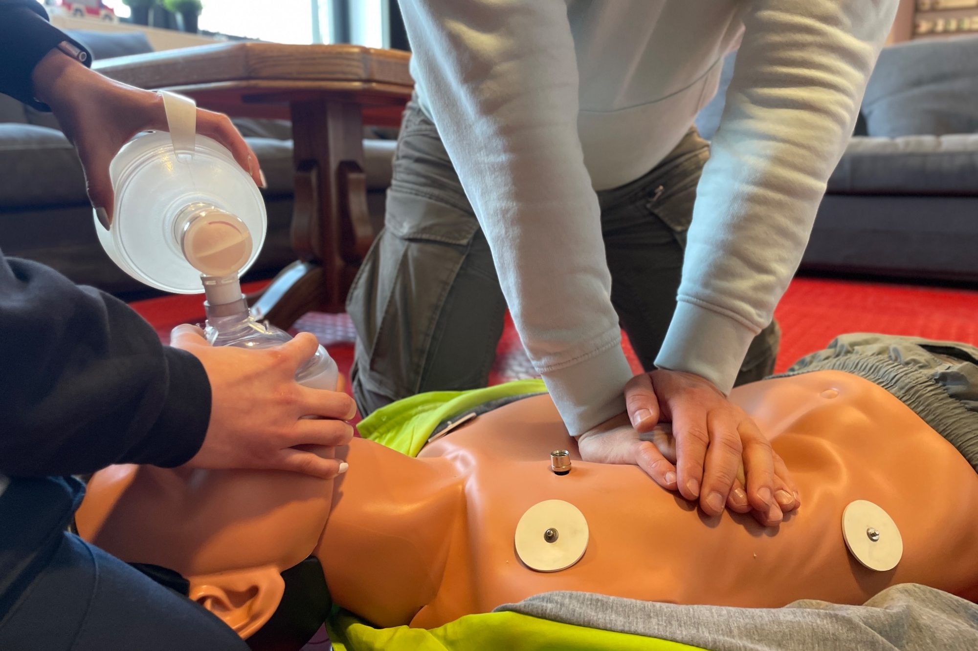 Zwei Personen üben die CPR an einem Dummy. Ein Beatmungsbeutel kommt zum Einsatz