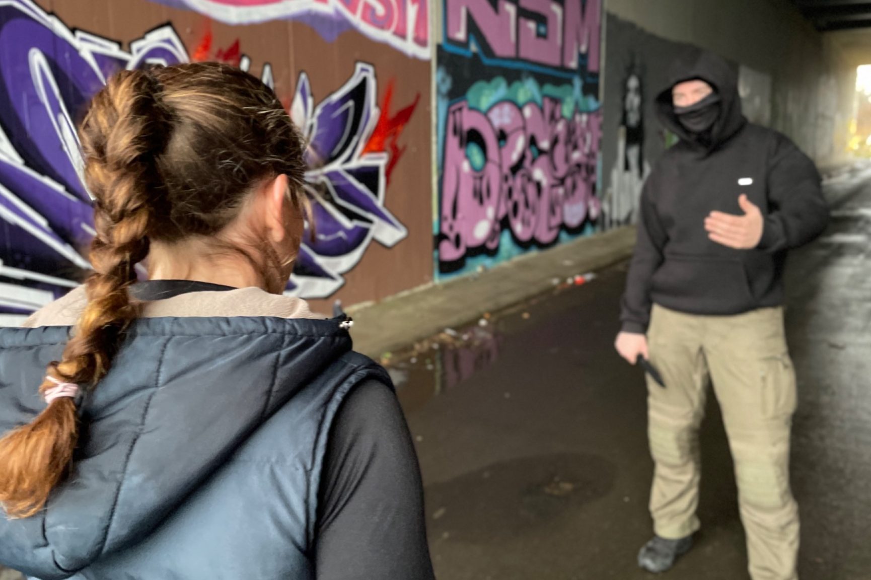 Ein bewaffneter Mann bedroht eine junge Frau in einem Tunnel mit Graffiti an den Wänden mit einem Messer 